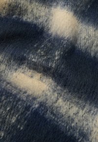 Vuna deka s plavim i krem uzorkom. Mekana, teksturirana površina s apstraktnim svijetlim i tamnim točkama. Pravilnog je pravokutnog oblika.