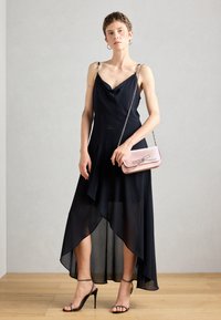 Robe noire avec un décolleté drapé, un ourlet asymétrique et un tissu transparent ; associée à un sac à main rose orné d'un nœud et d'une bandoulière en chaîne argentée.
