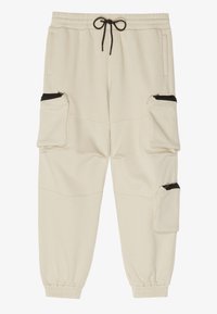 Beige Jogginghose mit elastischem Bund und Bündchen, schwarzem Kordelzug, zwei seitlichen Reißverschlusstaschen und zwei regulären Seitentaschen.