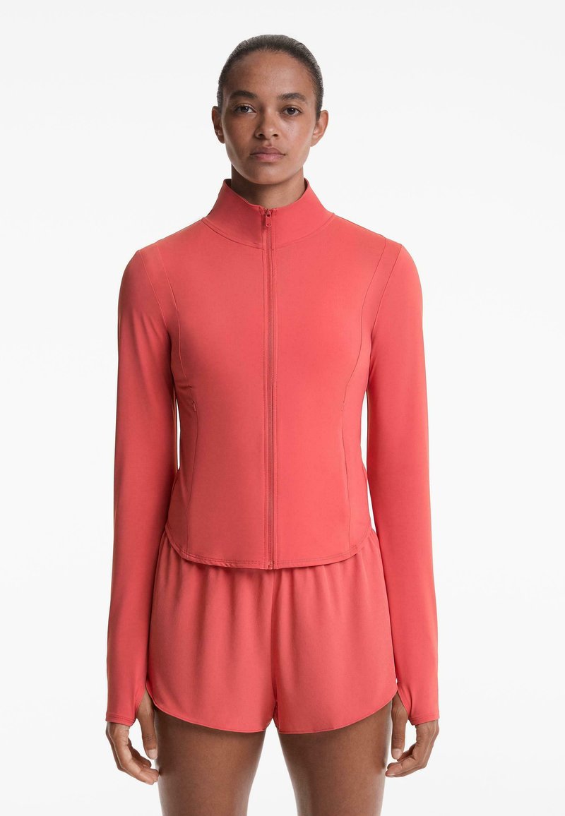 Koraal sporttop met een hoge kraag, volledige rits en lange mouwen, gecombineerd met bijpassende shorts. Glad, aansluitend materiaal met minimale naden.