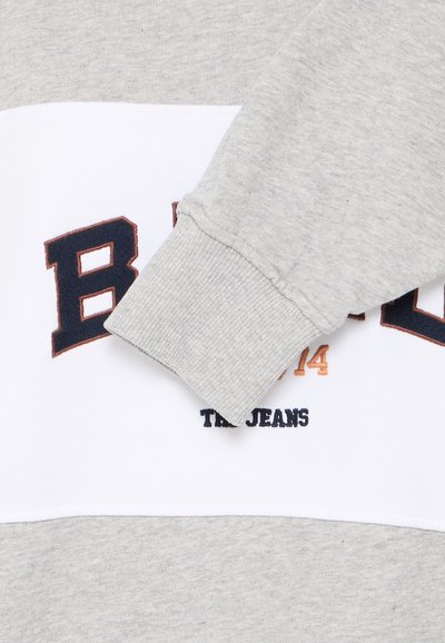 Felpa grigia con una fascia orizzontale bianca su cui sono ricamati in blu navy scuro e arancione "BRAND" e "THE JEANS". Dettagli a coste ai polsi.