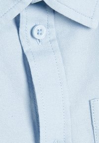 Camicia button-up azzurro chiaro con colletto strutturato, tasca sul petto e tessuto testurizzato con dettagli di cucitura visibili.