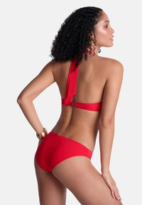 Bikini rouge avec un design à encolure halter et un lien au dos. Tissu lisse avec une couverture minimale et un accent doré au niveau de la taille.