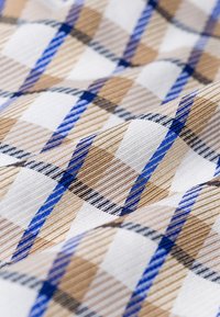 Tissu avec un motif à carreaux beige, bleu, noir et blanc montrant la texture et les plis.