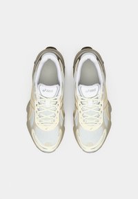 Athletic shoes in white mesh with beige accents, reflective detailing, and a textured sole. Features traditional lacing and logo on the tongue.