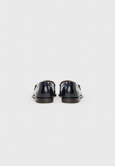 Donkere lederen schoenen met een gladde afwerking, met een afgeronde vorm en een lage hak. Details omvatten een gespaccent en een bruine binnenvoering.