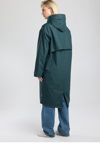 Imperméable vert foncé avec capuche, coupe décontractée, dos fendu et manches longues. Matière texturée avec détails de couture.