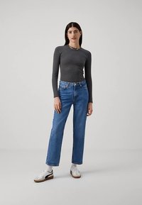 Gray long-sleeve top paired with blue straight-leg jeans and white sneakers, featuring a simple design and a fitted silhouette.