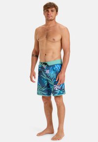 Badrumshorts med ett blått tropiskt bladmönster, med inslag av grönt och rosa, ett elastiskt midjeband och en snörning.