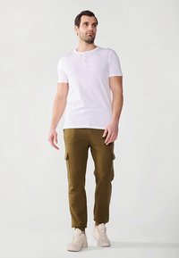 Vit kortärmad henleytröja kombinerad med olivgröna cargobyxor med sidofickor och ljusbeige sneakers.