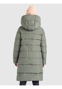 Long puffer coat in muted green, featuring a hood, quilted design, and side logo patch. Worn with a light pink knit beanie.