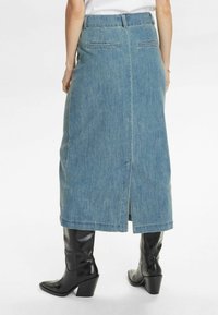 Gaiši zilā džinsa svārki ar taisnu formu, aizmugures šķirba un jostas cilpiņām. Saderēti ar melniem zābakiem ar papēžiem. Parādīts aizmugures skats.