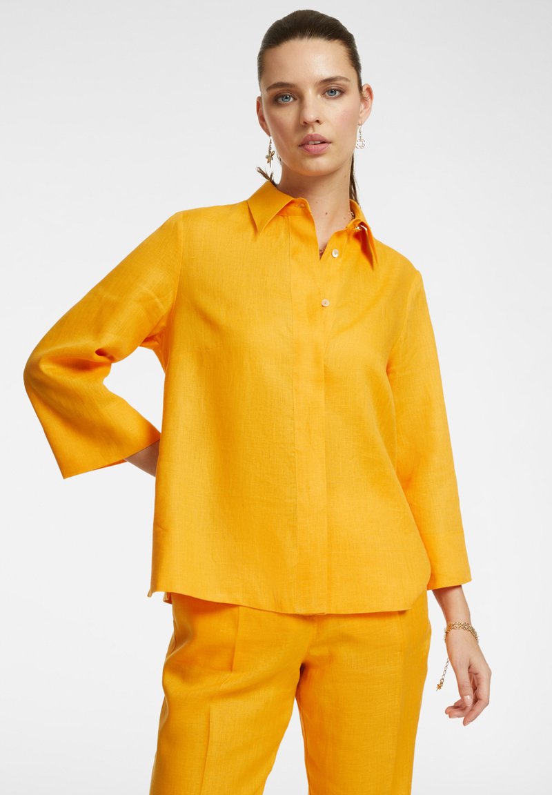 Camicia di lino gialla con colletto a bottoni, maniche a tre quarti e vestibilità rilassata, abbinata a pantaloni gialli coordinati.