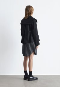 Black wool blend jacket with a collar, paired with a knee-length black and white striped skirt. Worn with black loafers and socks.