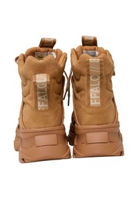 Zapatillas altas de gamuza en color marrón claro con una suela de goma gruesa, que cuentan con un prominente tirador en el talón y un detalle de marca en la parte trasera.