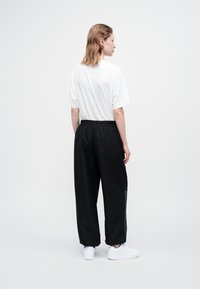 Schwarze, locker sitzende Hosen mit elastischem Bund und Seitentaschen, kombiniert mit einem weißen, kurzärmligen Hemd und weißen Turnschuhen.