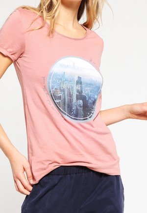 Rosa T-Shirt aus weicher Baumwolle mit rundem Ausschnitt. Mit einem kreisförmigen Grafikdesign einer Stadtsilhouette, ergänzt durch stilisierten Text.