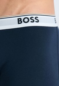 Navy blue boxer shorts with a soft, stretchy fabric. Features a wide elastic waistband with "BOSS" logo in black and white accent stripes.