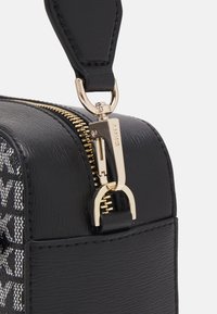 La borsa nera in tessuto presenta una cerniera dorata, un attacco per la tracolla in pelle e un accento di tessuto con motivo distintivo su un lato.