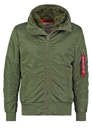 Giacca bomber verde oliva con zip frontale, cappuccio foderato in pelliccia, polsini e orlo a coste, e una tasca laterale con un'etichetta di stoffa rossa.