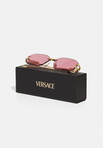 Ochelari de soare Versace cu lentile roz, accente aurii și carcasă rectangulară neagră. Au un design geometric al ramei și accesorii texturate.