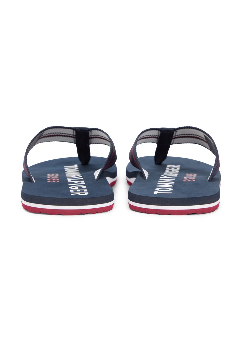 Par de sandalias de dedo azul marino con tiras a rayas blancas y rojas, logo de Tommy Hilfiger en las plantillas y suelas en capas de rojo, blanco y azul marino.