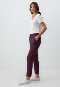 T-shirt blanc à col en V, ajusté, associé à un pantalon bordeaux fuselé avec des poches latérales et une texture lisse, complété par des baskets blanches.