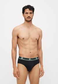 Sorte bomullsboxer med en grønn PUMA-logo i livet, med en tettsittende design og glatt tekstur. Modell som viser forfra.