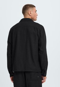 Zwarte shirtjacket van textuurstof, met een puntige kraag, lange mouwen met knoopsluitingen en een ontspannen pasvorm.