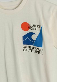 White shirt with a blue sailboat and wave graphic, red sun, and text "Club de Voile Côte d'Azur St. Tropez" on the chest.