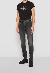 Černé bavlněné tričko s logem "Calvin Klein Jeans", kombinované se světlejšími černými džínami a černými teniskami, doplněné černým opaskem.