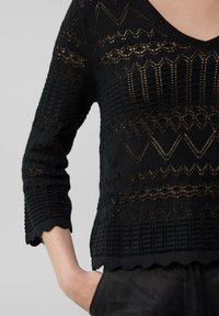 Schwarzer Strickpullover mit strukturierten Mustern, ausgestattet mit einem gewellten Saum und Dreiviertelärmeln, die eine Mischung aus offenen und geschlossenen Maschenmustern zeigen.