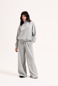 Γκρι φλις πουλοβερ με φερμουάρ μέχρι το ένα τέταρτο και μπροστινή τσέπη, σε συνδυασμό με αντίστοιχο φαρδύ παντελόνι φόρμας. Μαλακή υφή με ελάχιστα σχεδιαστικά στοιχεία.