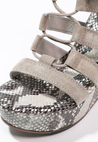 Sandale à talon avec des brides en daim beige, plateforme à imprimé serpent, surface texturée, design à bout ouvert et talon arrondi.