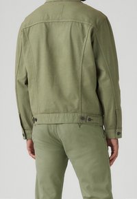 Chaqueta verde oliva con un diseño casual, que presenta botones en los puños y en la parte inferior, hecha de una tela texturizada y duradera.