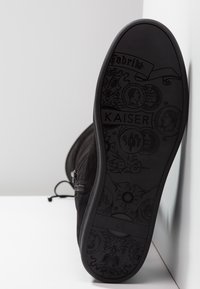 Chaussure en daim noir avec une semelle en caoutchouc texturée présentant un embossage complexe. Comprend un détail de fermeture éclair sur le côté.