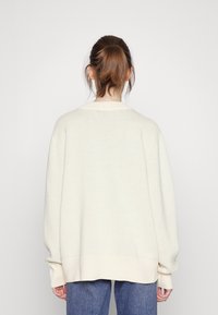 Roomkleurige oversized trui met een brede halslijn en lange, taps toelopende mouwen, met een zachte gebreide textuur en een geribbelde zoom.