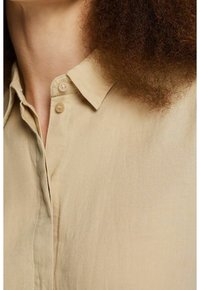 Beige shirt with a collar, featuring two buttons and a front placket. The fabric appears lightweight with a smooth, slightly textured finish.