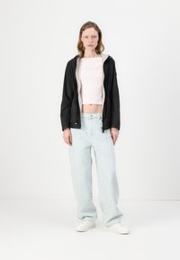 Jaqueta leve preta com forro cinza, camisa curta rosa com texto em relevê, e jeans soltos azul claro com bordado floral. Ténis brancos.