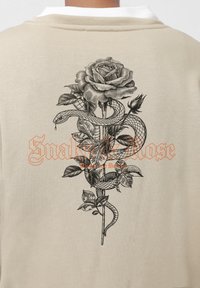 Beige sweatshirt featuring a black rose and snake graphic on the back, with orange text reading "Snake & Rose" underneath the design.