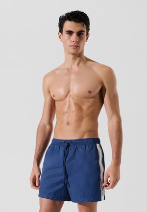 Marineblaue Badehorts aus leichtem Material, mit einer verstellbaren Taille und weißen Seitenstreifen mit Logo-Details. Angenehme Haptik.