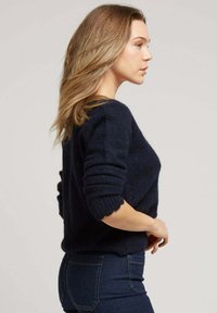 Un pull en maille bleu marine, avec un col rond et des poignets retournés, associé à un jean slim noir. Texture douce et coupe décontractée.