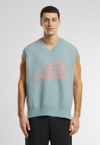 Lyseblå ærmeløs sweater med V-udskæring, der har en blød tekstur og et grafisk design i pink, som står "another" på forsiden.