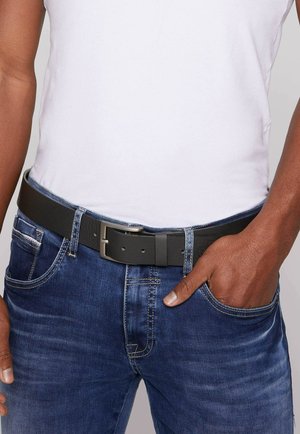 Black leather belt with a silver buckle worn over blue denim jeans. The fabric is slightly distressed, providing a textured appearance.
