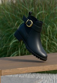 Schwarzer Knöchelstiefel aus glattem Leder, ausgestattet mit einer goldenen Schnalle, strukturiertem Design und einer robusten Sohle mit Griffmustern.