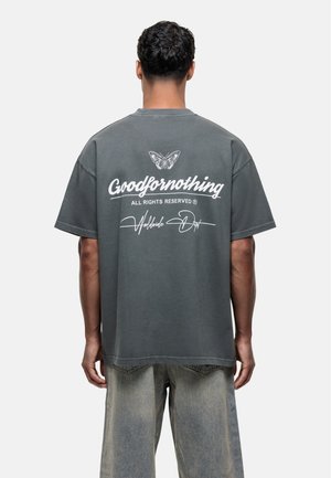 Grijs oversized T-shirt met een vlinderafbeelding en witte tekst "Goodfornothing" op de achterkant. Van katoen met een relaxte pasvorm.