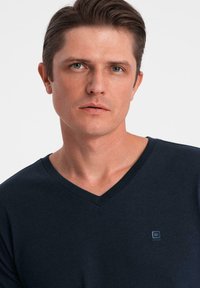 Námořnicky modré tričko s výstřihem do V vyrobené z měkké bavlny, s malým logem na hrudi, hladkou texturou a pohodlným střihem.