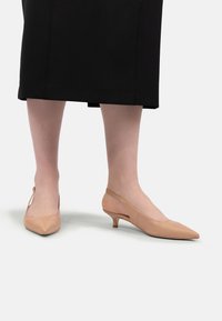 Sandale bej cu toc slingback, cu vârful ascuțit, toc kitten joasă și textură din piele netedă. Accentuate cu spate deschis și detalii minime.