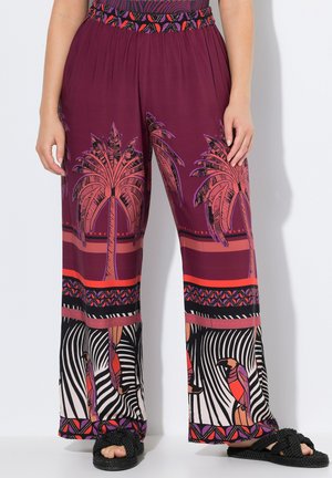 Pantaloni a gamba larga in un tessuto bordeaux scuro caratterizzati da motivi di palme e uccelli. Accentuati da una cintura colorata e sandali neri.