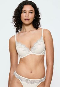 Kremowy biustonosz z koronkowym wykończeniem i pasującymi majtkami, z falbaniastymi krawędziami, gładką fakturą oraz regulowanymi ramiączkami z subtelnym wzorem.